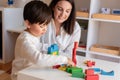 Preschooler Kid playing with wood blocks and teacher educador help. Homeshooling. Learning Community. Montessori School