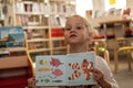 Preschooler little girl sitting and reading a book in library. Kid with books near a bookcase. Happy, cheerful and cute girl read Royalty Free Stock Photo