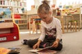 Preschooler little girl sitting and reading a book in library. Kid with books near a bookcase. Happy, cheerful and cute girl read Royalty Free Stock Photo