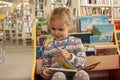 Preschooler little girl sitting and reading a book in library. Kid with books near a bookcase. Happy, cheerful and cute girl read Royalty Free Stock Photo