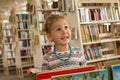 Preschooler little girl sitting and reading a book in library. Kid with books near a bookcase. Happy, cheerful and cute girl Royalty Free Stock Photo