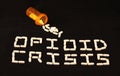 Opioid crisis spelled out with with white pills on a black background with spilled pills above the words.