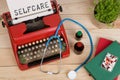 medical diagnosis - doctor workplace with blue stethoscope, pills, red typewriter with text Selfcare