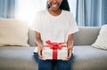 Present, box and woman on a sofa in the living room with a giving gesture for celebration or event. Bow, wrapping paper Royalty Free Stock Photo