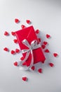 Present box is wrapped in red paper with silver ribbon bow. White background with a pile of red jelly hearts. Top view. Royalty Free Stock Photo