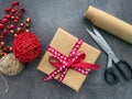 Present, Craft paper roll, scissors, twine, red berries and christmas decoration on wooden table.