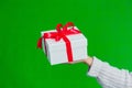 Close up of female hand holding white gift box tied with red ribbon isolated on green background. Royalty Free Stock Photo