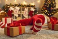 Gift box tied with red ribbon beside tired drunk Santa lying asleep on floor in living room