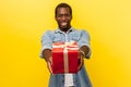 Present for you! ! Portrait of positive generous man giving red gift box. isolated on yellow background