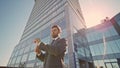 Presentable businessman adjusting suit on sunny street near modern skyscraper.