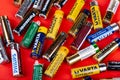 Presentation of different popular brands of AA batteries scattered all around on a red background. Lots of various small batteries