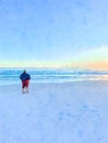 A woman on a sandy beach looking at the sunset and sea.