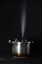 Pressure cooker releasing steam through the lid, against a black background