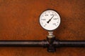 Pressure gauge on a background of a rusty old iron wall and a black pipe Royalty Free Stock Photo