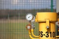 Pressure gauge for measuring the pressure of natural gas in a gas pipeline. Yellow transport pipes on the surface of the fence.