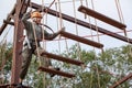 Preteen beautiful girl climbs on rope harness in summer wood park