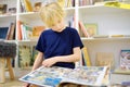 A preteen boy leafing through a book while sitting at the bookshelves at home, in a school library or bookstore. Smart kid reading Royalty Free Stock Photo