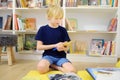 A preteen boy leafing through a book while sitting at the bookshelves in a school library or bookstore. Smart kid reading Royalty Free Stock Photo