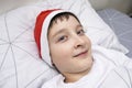 A preteen boy lying in bed in santa hat during christmas eve night and waiting for gifts and miracles, happy xmas and new year Royalty Free Stock Photo