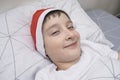 A preteen boy lying in bed in santa hat during christmas eve night and waiting for gifts and miracles, happy xmas and new year Royalty Free Stock Photo