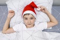 A preteen boy lying in bed in santa hat during christmas eve night and waiting for gifts and miracles, happy xmas and new year Royalty Free Stock Photo