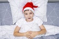 A preteen boy lying in bed in santa hat during christmas eve night and waiting for gifts and miracles, happy xmas and new year Royalty Free Stock Photo