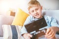 Preteen boy plays with smartphone connected with gamepad lying on the cozy sofa in the home living room