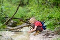 Preteen boy in red shirt is exploring nature and playing with water in brook during hiking in mountains valley. Active leisure for Royalty Free Stock Photo