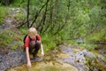 Preteen boy in red shirt is exploring nature and playing with water in brook during hiking in mountains valley. Active leisure for Royalty Free Stock Photo