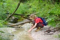 Preteen boy in red shirt is exploring nature and playing with water in brook during hiking in mountains valley. Active leisure for Royalty Free Stock Photo