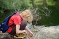 Preteen boy in red shirt is exploring nature and playing with water in lake during hiking in mountains valley. Active leisure for Royalty Free Stock Photo