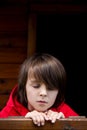 Preteen boy in red sweatshirt, hiding behind a wooden door, looking scared Royalty Free Stock Photo