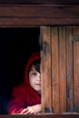 Preteen boy in red sweatshirt, hiding behind a wooden door, looking scared Royalty Free Stock Photo