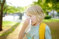 Preteen boy sneezing and wipes nose with napkin during walking in summer park. Flu season and cold rhinitis. Allergic kid Royalty Free Stock Photo