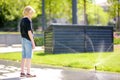 Preteen boy watching an automatic garden sprinkler during walks in a public park. Gardening equipment. Watering the grass on lawn