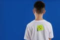 Preteen boy with winking face sticker on back against background, space for text. April fool`s day