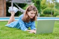 Preteen girl lying on grass in backyard using laptop for relaxing and studying Royalty Free Stock Photo