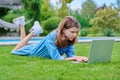 Preteen girl lying on grass in backyard using laptop for relaxing and studying Royalty Free Stock Photo