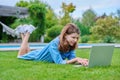 Preteen girl lying on grass in backyard using laptop for relaxing and studying Royalty Free Stock Photo