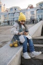 Preteen girl sitting on street stairs and texting with smartphon