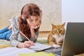 Preteen girl studying at home with ginger cat using laptop Royalty Free Stock Photo