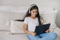 Preteen girl wear headphones using modern digital tablet at home Royalty Free Stock Photo