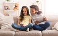 Preteen girls with gadgets sitting on sofa at home