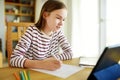 Smart preteen schoolgirl doing her homework with digital tablet at home. Education and distance learning for kids. Homeschooling