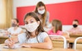 Preteen schoolgirl in protective face mask studying in classroom