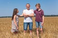 Preteen son and daughter looking at their single father, kids lay hands on his shoulders, wheat field