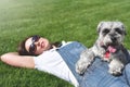 Pretty adult caucasian happy woman resting in the park on a sunny day with her beloved dog. Female lies on the grass, smiling and Royalty Free Stock Photo