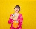 Pretty adult chubby woman with short hair holding colorful holiday eggs and a easter basket on yellow solid studio background