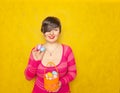 Pretty adult chubby woman with short hair holding colorful holiday eggs and a easter basket on yellow solid studio background