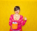 Pretty adult chubby woman with short hair holding colorful holiday eggs and a easter basket on yellow solid studio background